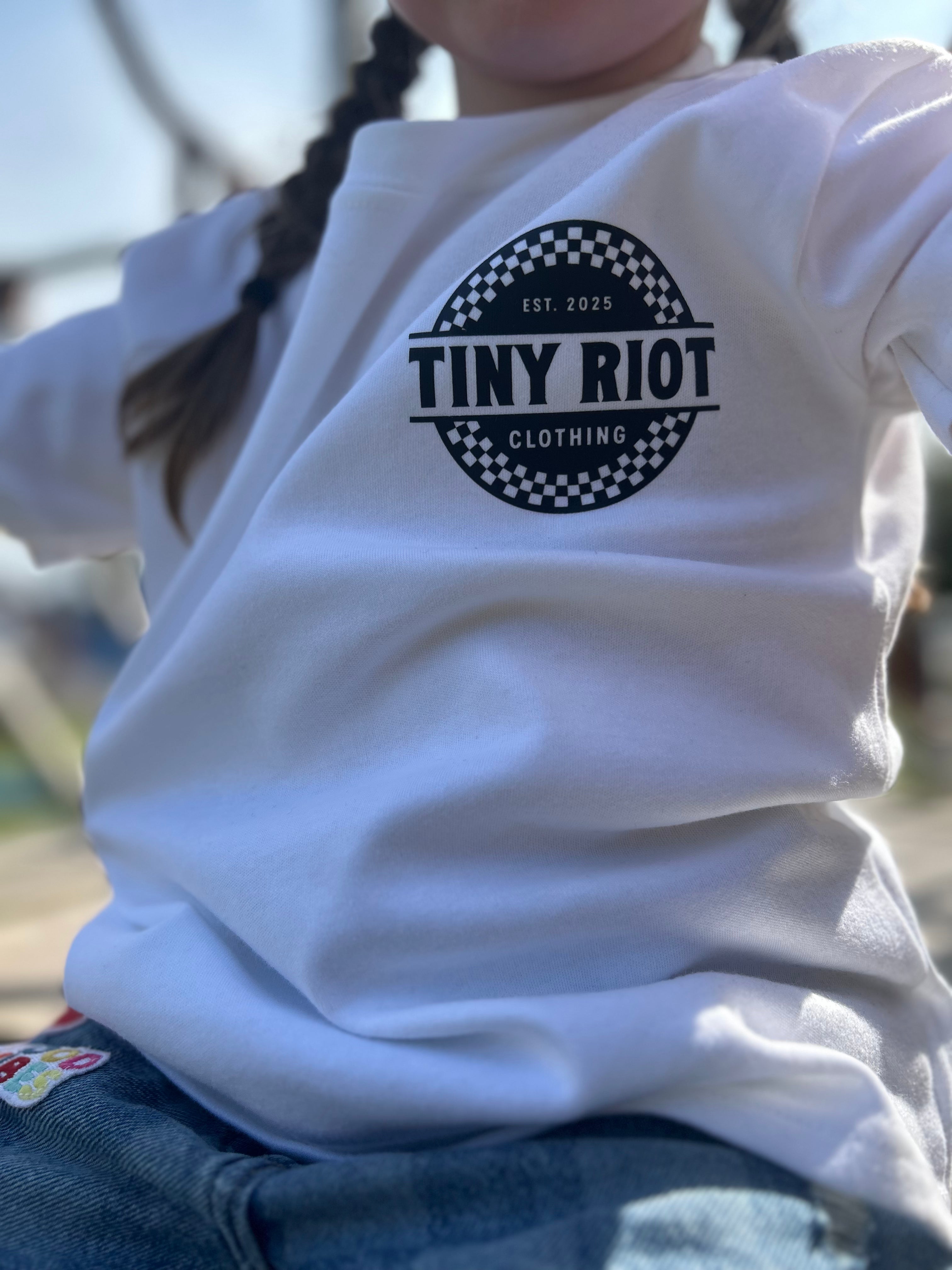 White t-tshirt with 'Tiny Riot' logo worn by a child outdoors